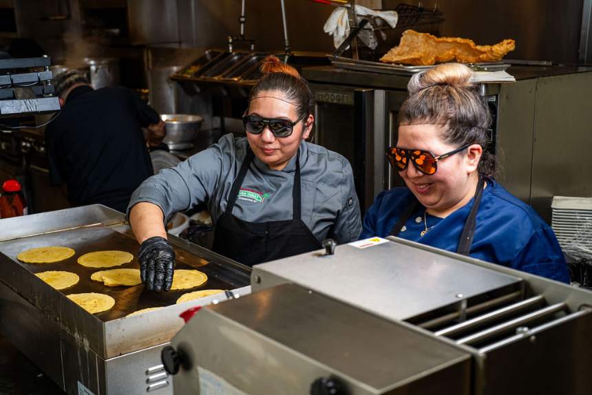 Two cooks pressing corn tortillas on the griddle in the kitchen