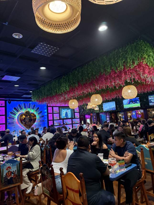 A full dining room at night, with the lit bar behind it