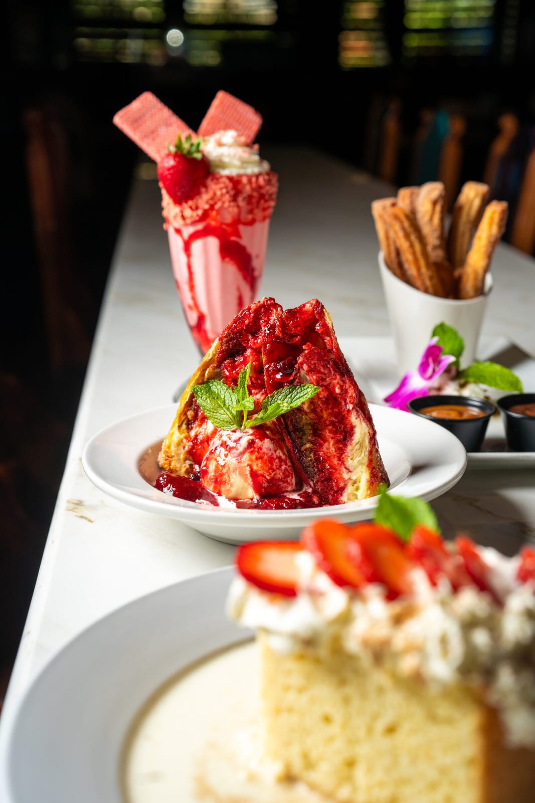 A spread of desserts laid out on a table: churros, tres leches and a layered strawberry sundae